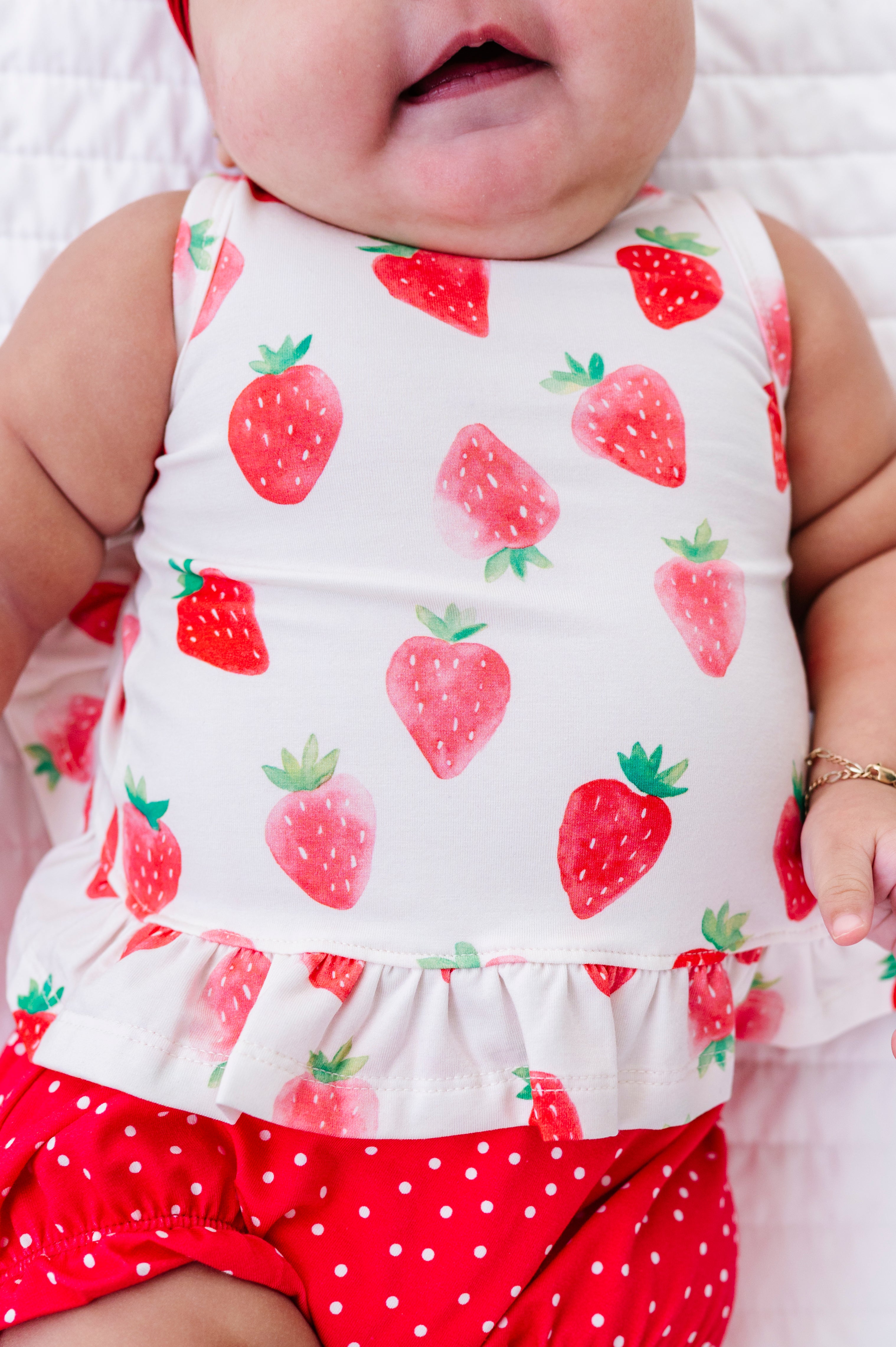 Baby wearing a sleeveless top with strawberry pattern and red polka dot bloomers.